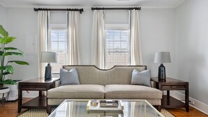 A living room with a sofa, two side tables, a glass coffee table, and a potted plant. - Chic 2 Bedroom Spring St Retreat - Walk to King St (Charleston)