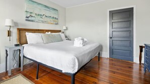A neatly made bed with white linens, a wooden headboard, and a painting of a seascape on the wall. - Chic 2 Bedroom Spring St Retreat - Walk to King St (Charleston)