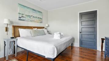 A neatly made bed with white linens, a wooden headboard, and a painting of a seascape on the wall.