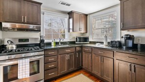 A kitchen with dark wooden cabinets, stainless steel appliances, a microwave, and a coffee maker. - Chic 2 Bedroom Spring St Retreat - Walk to King St (Charleston)
