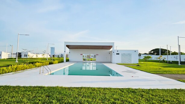 Un bâtiment moderne avec une piscine en premier plan, entouré d’une pelouse bien entretenue et de quelques arbres.