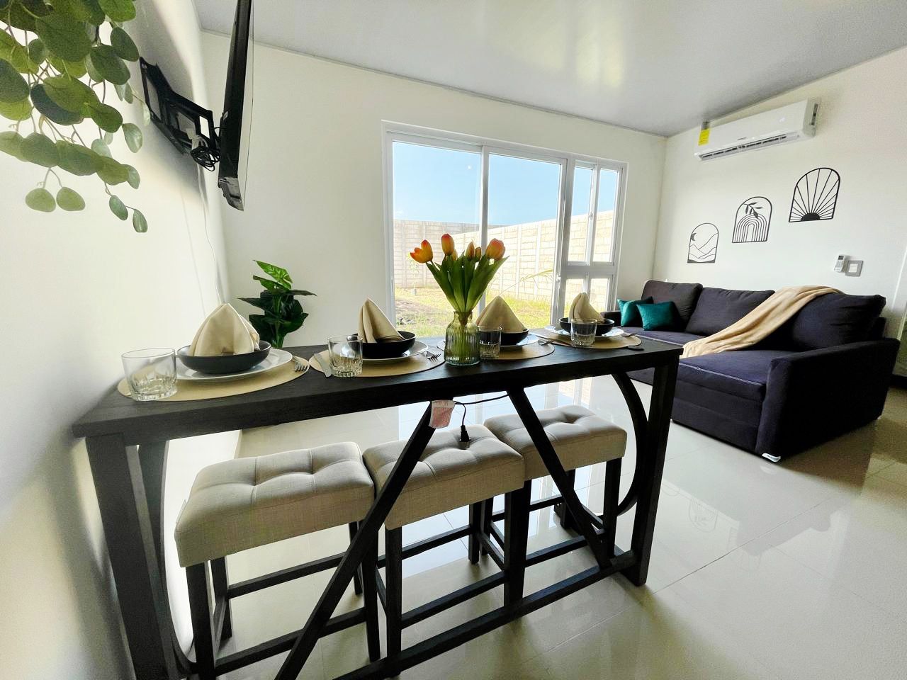 Un coin repas avec une table dressée pour quatre personnes, un canapé et une fenêtre donnant sur un beau paysage.