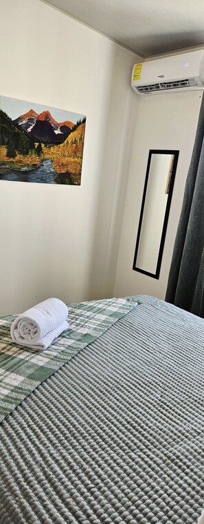 Une chambre d’hôtel avec un lit, un tableau représentant un paysage de montagne, un climatiseur, un miroir et une serviette enroulée.