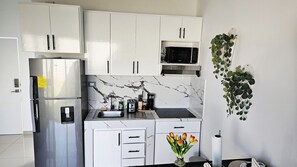 Una cucina moderna con mobili bianchi, un frigorifero in acciaio inossidabile, un forno a microonde e un lavello con pannello paraschizzi in marmo.
