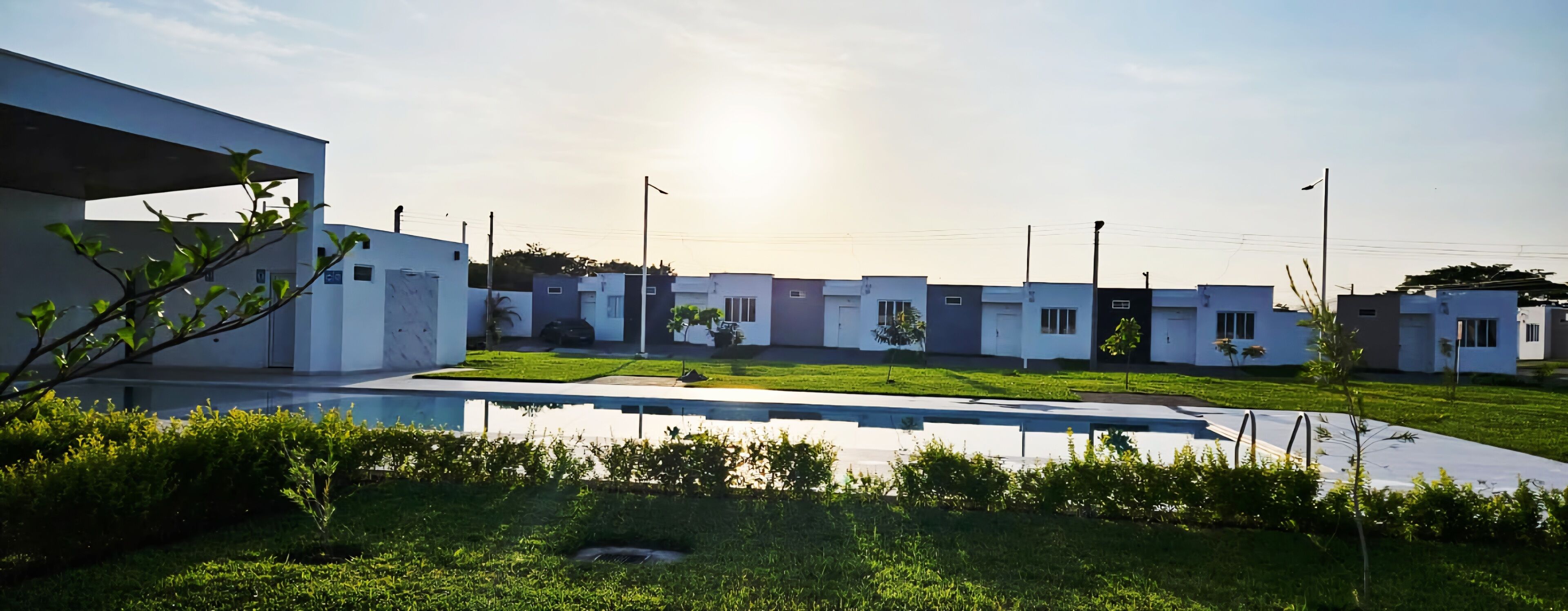 Un área residencial moderna con piscina, casas de arquitectura uniforme y cielo despejado.
