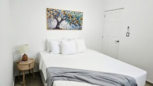 Une chambre d’hôtel avec un lit, une table de chevet avec une lampe, un tableau au mur et une porte.