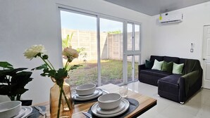 Une cuisine moderne avec un coin repas, une porte-fenêtre coulissante donnant sur un jardin, un canapé noir avec des coussins verts et un réfrigérateur blanc.