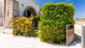 Ein Gebäude mit heller Fassade, einem Bogenportal und einem kleinen Garten mit Grün- und Rotpflanzen.