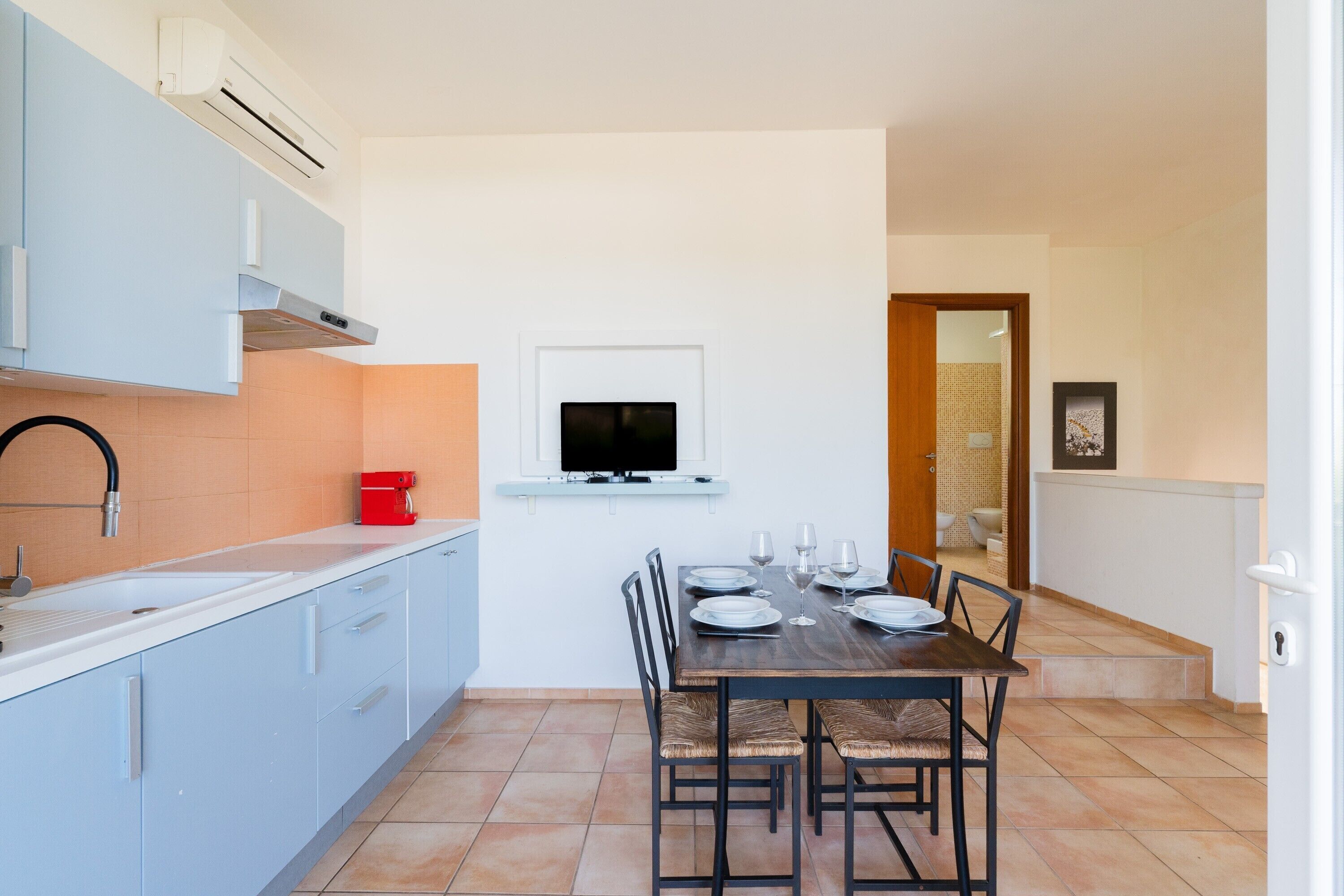 A compact kitchen with a dining area, a TV mounted on the wall, and a red coffee machine.