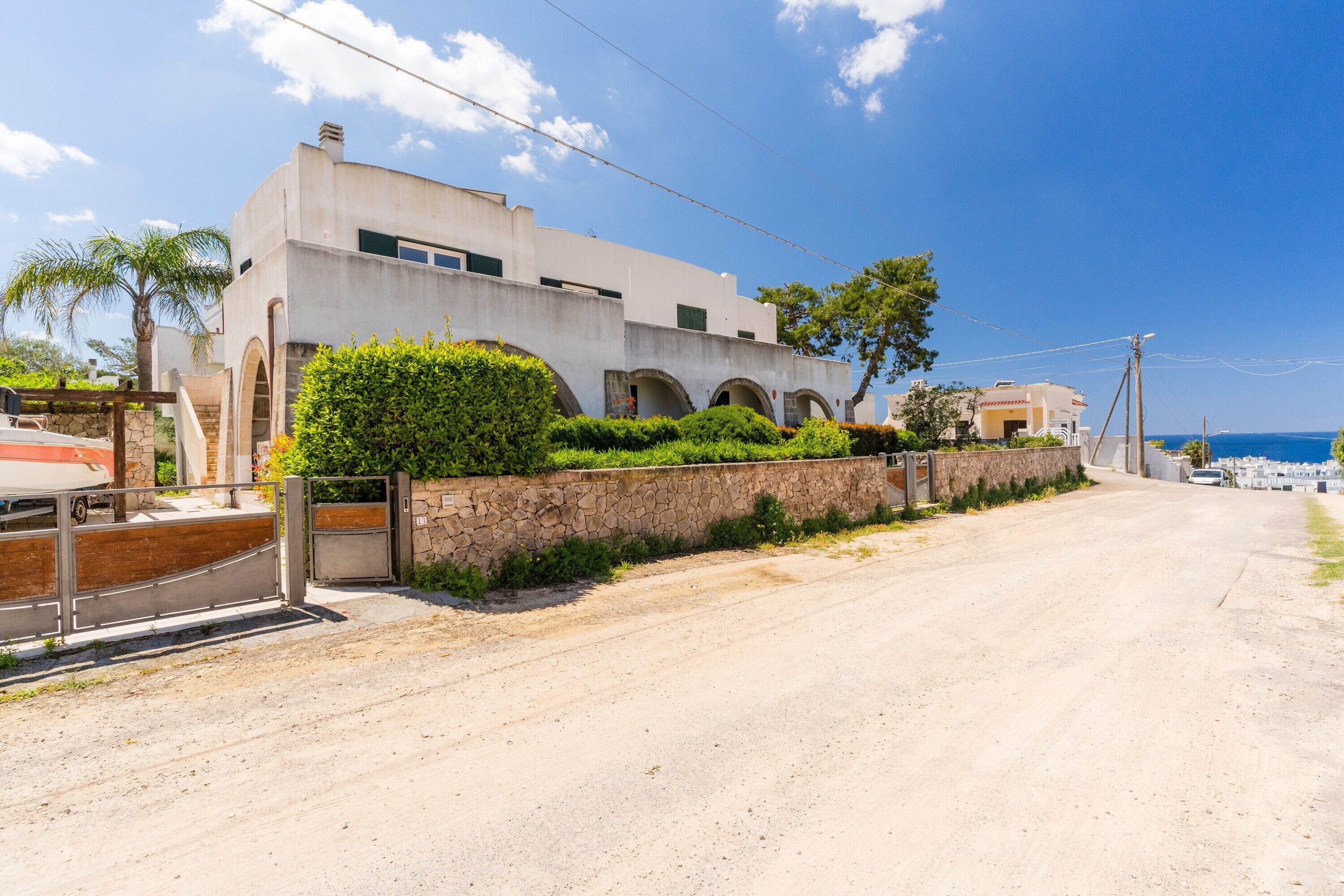 Una strada costiera con un edificio moderno, un muro in pietra e cielo sereno.