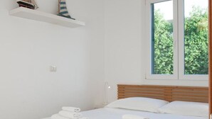 Ein Schlafzimmer mit einem Bett, weißen Handtüchern, einer Pendelleuchte, einem Fenster und einem Regal mit Modellschiffen.