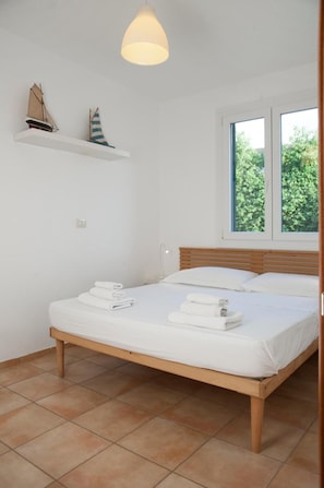 A bedroom with a bed, white towels, a hanging light fixture, a window, and a shelf with model ships. - Quattro Colonne 3 Apartment with Sea View (Santa Maria al Bagno)