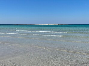 A beach with clear water, pebbly shore, and a distant landmass.