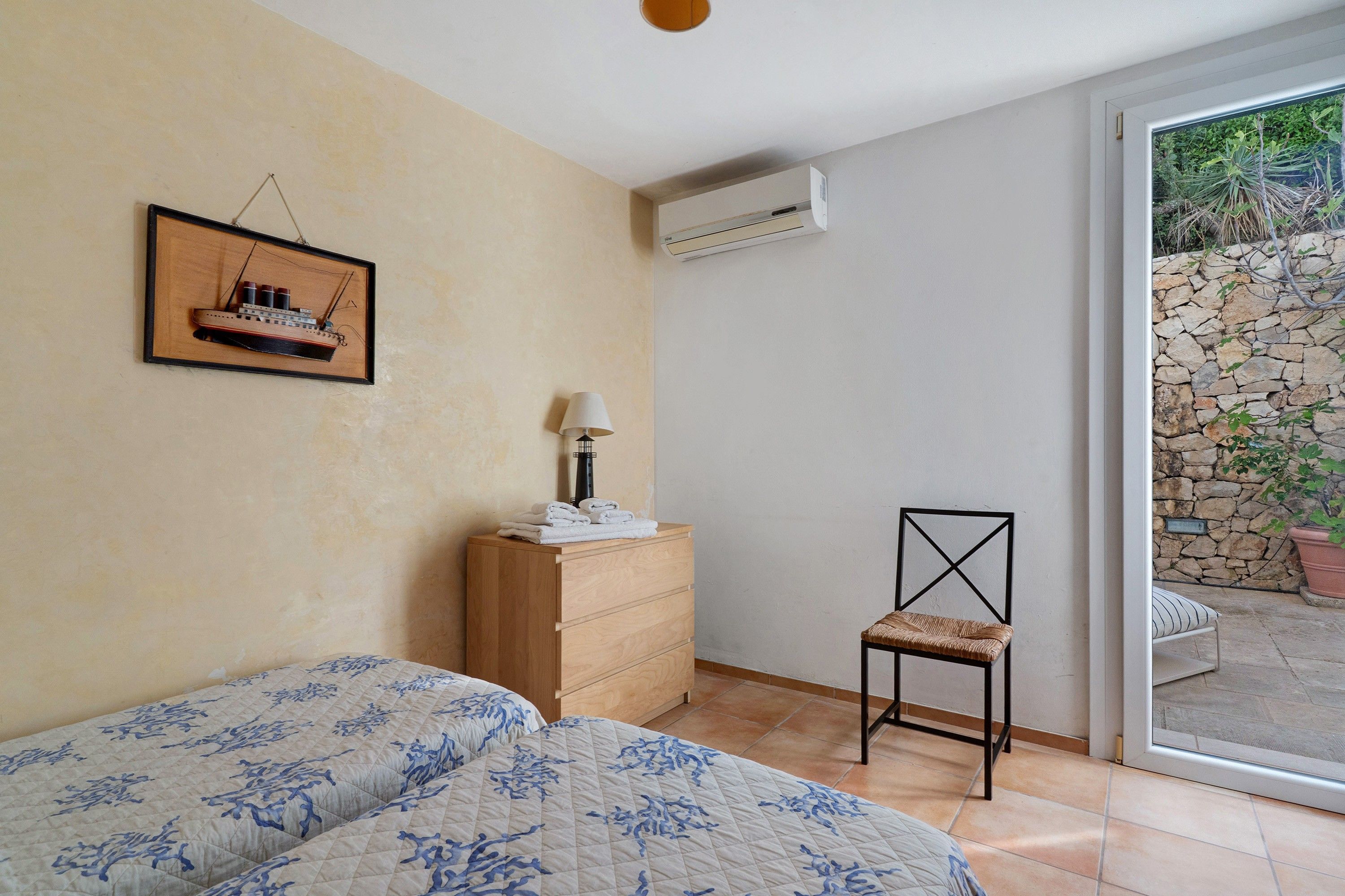 A bedroom with a bed, a dresser, a chair, and a wall-mounted air conditioner.