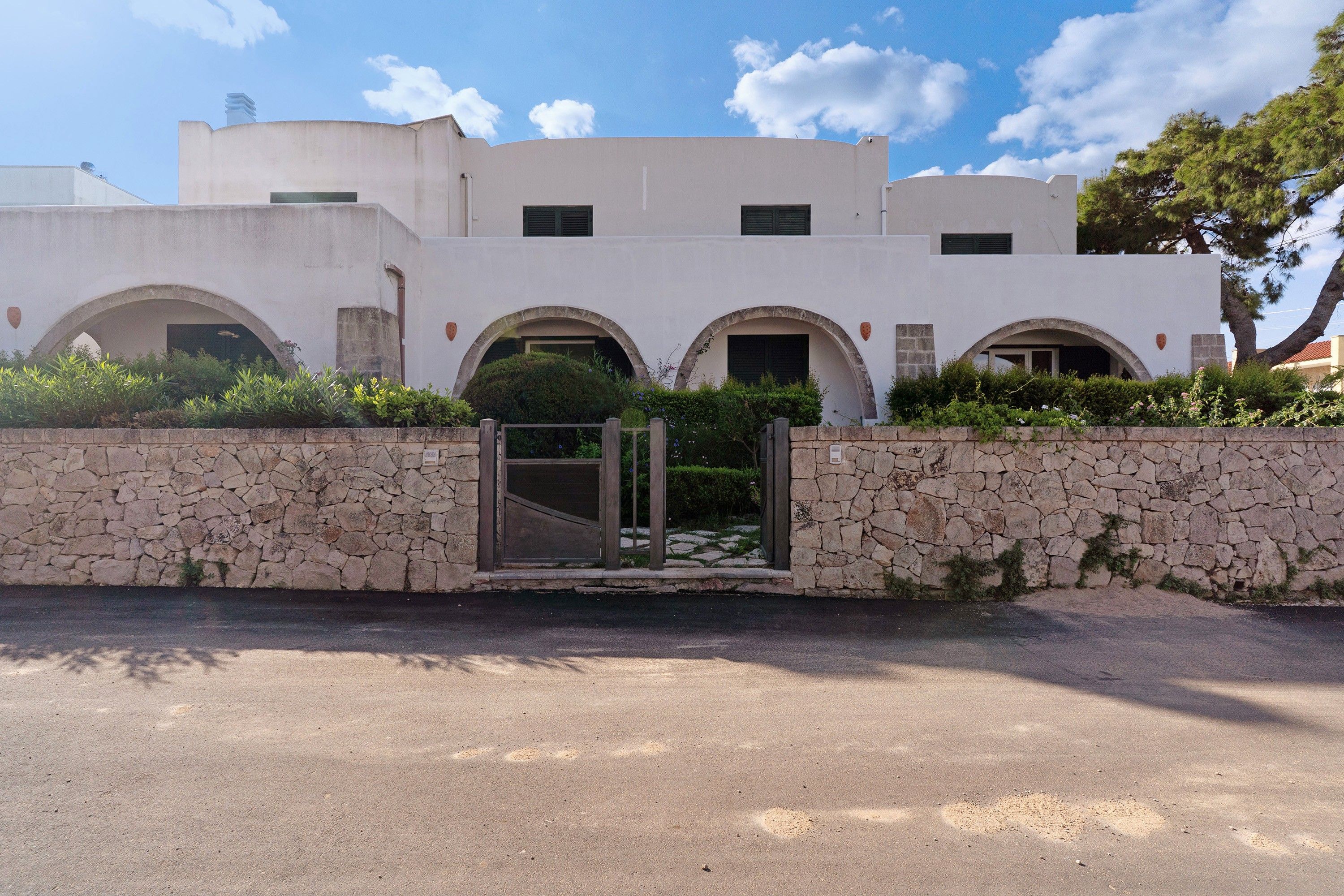 Ein Gebäude mit weißer Fassade, mehreren Rundbogenportalen und einer Mauer im Vordergrund.