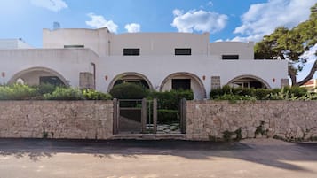 Ein Gebäude mit weißer Fassade, mehreren Rundbogenportalen und einer Mauer im Vordergrund.