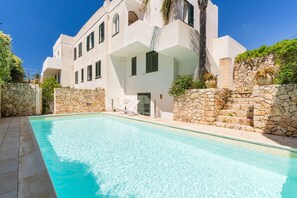 A modern building with a swimming pool, stone walls, and a clear blue sky.