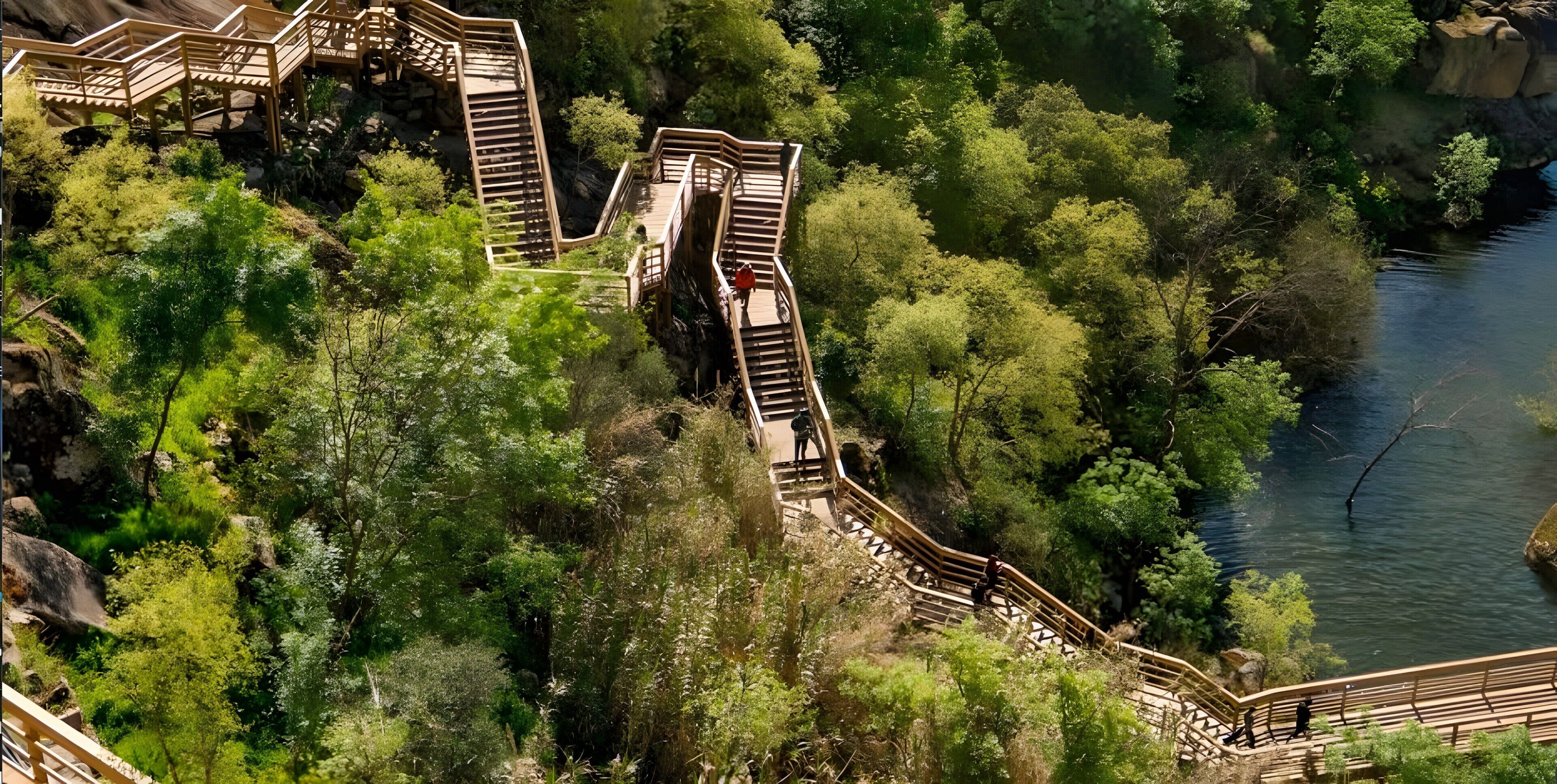 A wooden staircase leading to a viewing platform with a river and dense greenery in the background.