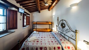 A bedroom with a bunk bed, wooden ceiling beams, a ceiling fan, a wall-mounted TV, and a window with a view.