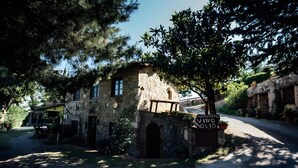 A rustic stone building with a wooden balcony, a gravel path, and a signboard.