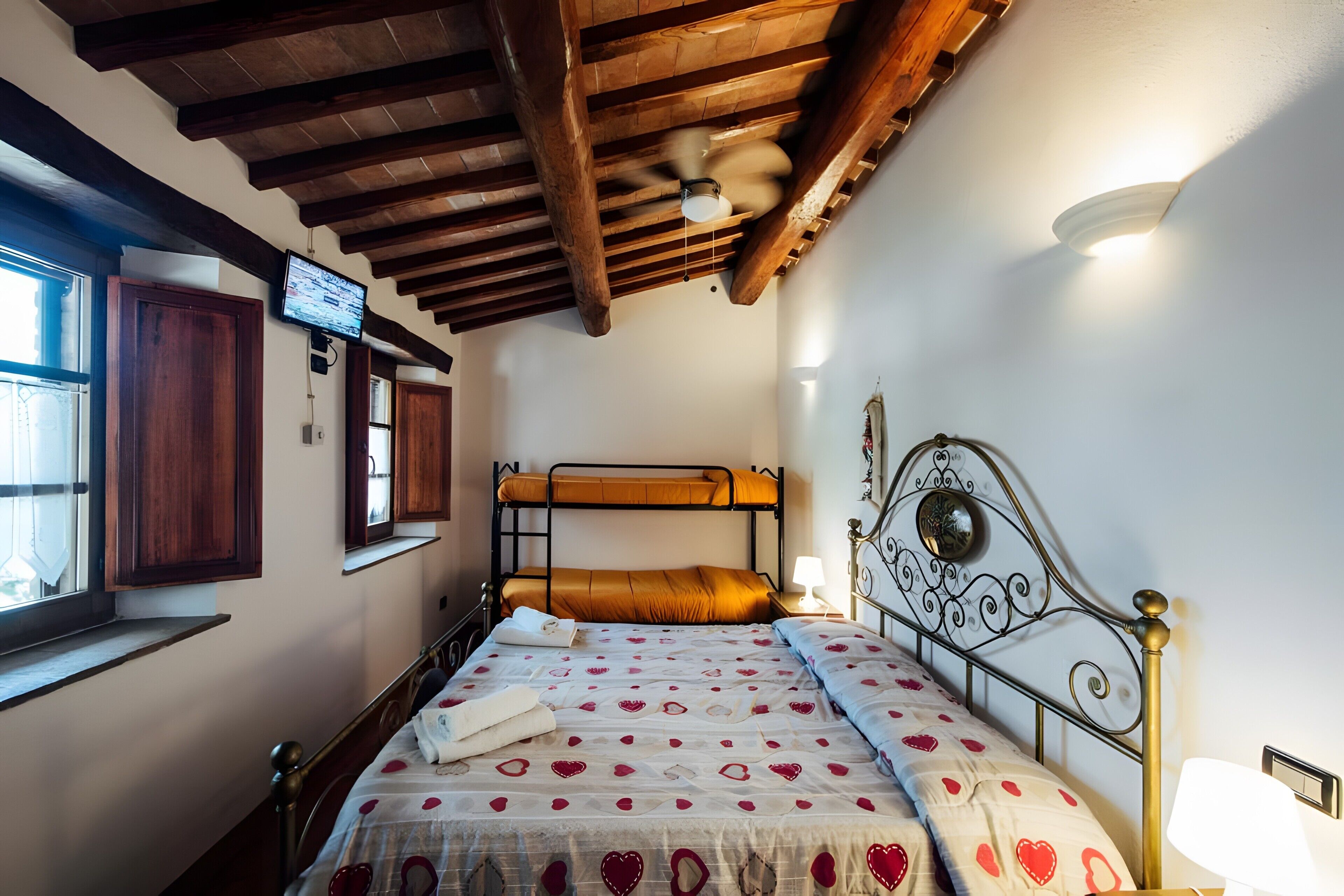 Une chambre avec un lit superposé, des poutres en bois au plafond, un ventilateur de plafond, un téléviseur fixé au mur et une fenêtre avec vue.
