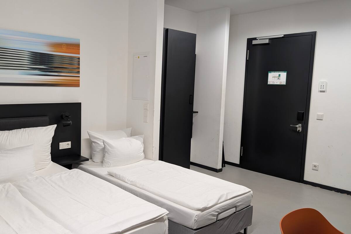 Ein Hotelzimmer mit zwei Betten, einem Nachttisch, einer Wandleuchte und einer Tür mit einem Schild.