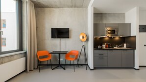 A modern kitchen with grey cabinets, a built-in microwave, and a small countertop. There is a dining area with a table and two orange chairs. A flat-screen TV is mounted on the wall. - Nena Apartments Moritzplatz by LESA (Berlin)