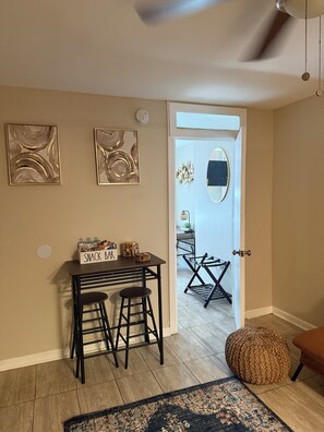 Habitación con barra de aperitivos, dos obras de arte abstracto en la pared, un espejo y un otoman tejido.