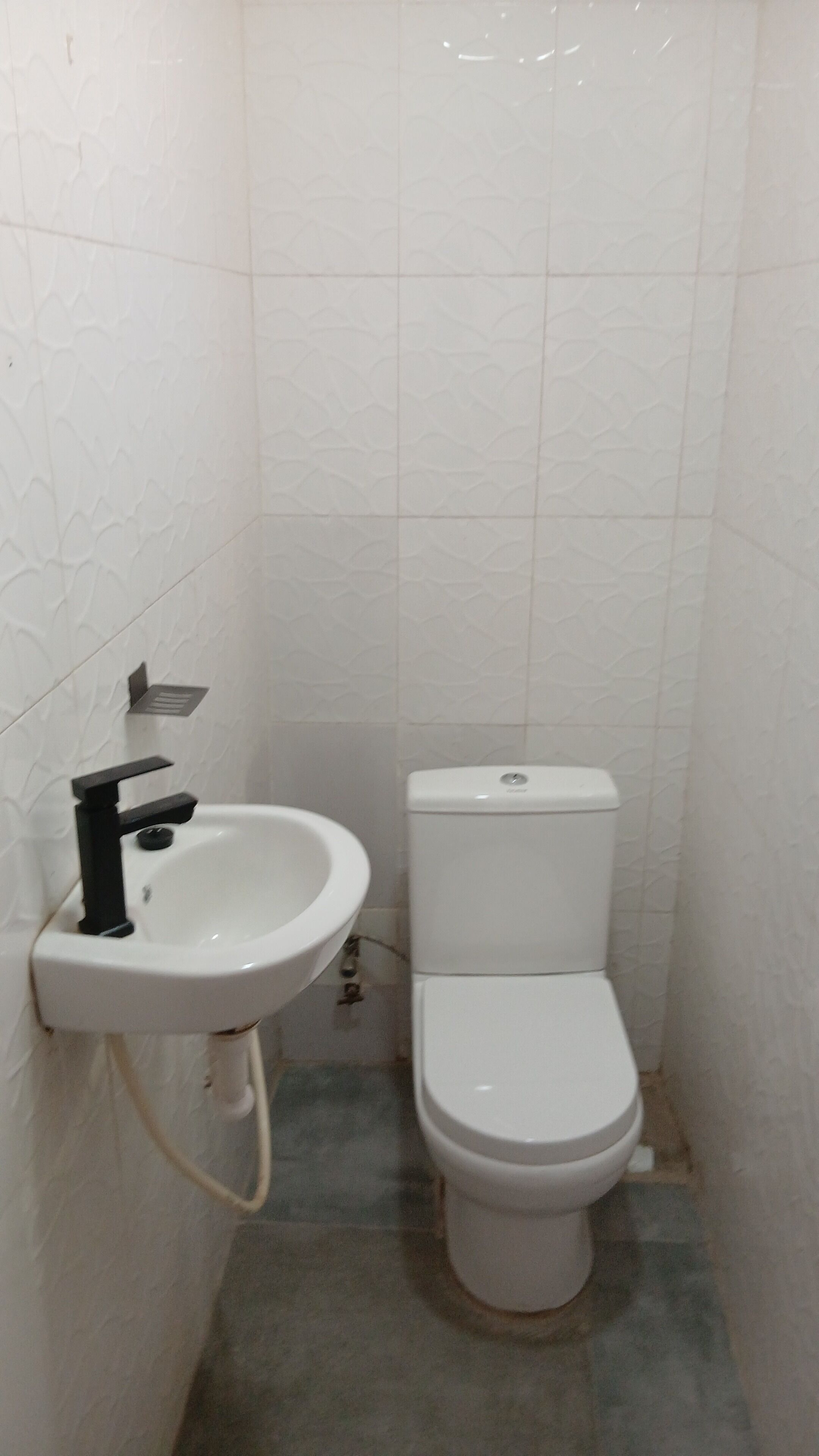 Un bagno piccolo con lavandino e water bianchi, pareti rivestite di piastrelle e uno scarico a vista.