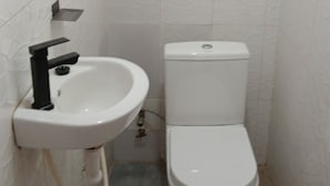 Pieni kylpyhuone, jossa on valkoinen pesuallas ja wc-istuin, laatoitetut seinät ja näkyvissä oleva viemäri.