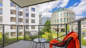 A balcony with a glass table and chairs, a view of surrounding buildings, and a clear sky. - Comfortable Apartment | Parking | Remote Work (Warszawa)