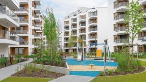 A residential building with multiple balconies, a playground with slides, and a small pool area. - Comfortable Apartment | Parking | Remote Work (Warszawa)
