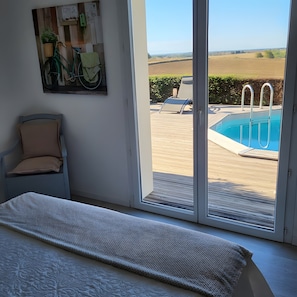 Ein Schlafzimmer mit großem Fenster, einem Bett, einem Sessel und einem Gemälde von einem Fahrrad.