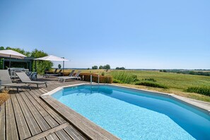 Una piscina con terraza de madera, sillas de descanso y sombrillas.