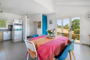 A dining area with a table set for two, a kitchen with a dishwasher and a refrigerator, and a view of the outdoors through a glass door. - Country House with Private Pool, Hot Tub, Wi-Fi and Air Conditioning in La Salvetat-Belmontet (La Salvetat-Belmontet)