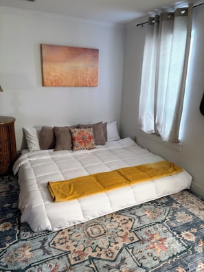 Un dormitorio con cama, un cuadro en la pared y una ventana con cortinas.