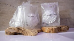 Two transparent plastic bags labeled 'shower cap' on a wooden surface. - Antica Piacenza (Piacenza)