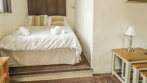 Uma cama bem arrumada com cabeceira, mesa de cabeceira com abajur e um pequeno banquinho de madeira.