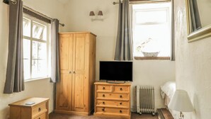 Quarto com guarda-roupa de madeira, televisão, mesa de cabeceira, luminária e janela com cortinas.