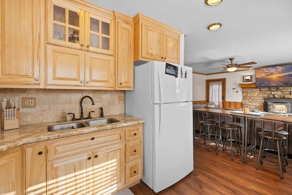 A kitchen with wooden cabinets, a white refrigerator, a stone fireplace, and a bar area with stools.