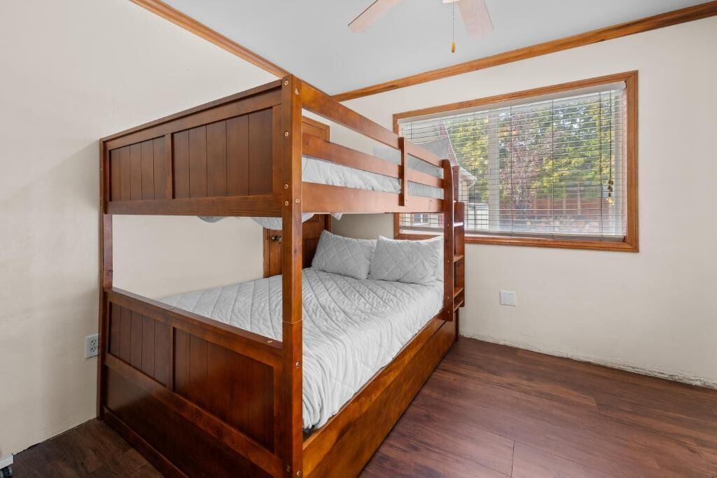 A bunk bed with a wooden frame, a window with blinds, and a ceiling fan.