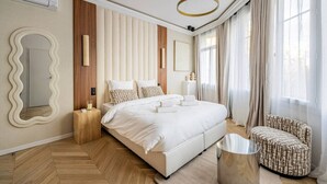A modern bedroom with a large bed, a round mirror, a wooden nightstand, and a patterned armchair. - Suite luxueuse-le Marais - Châtelet-Paris 3#AC (Paris)