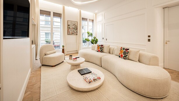 Un salon moderne avec un grand canapé d’angle beige, une table basse ronde et une petite table d’appoint.