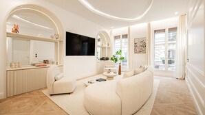 Un salon moderne avec un canapé, des fauteuils, un téléviseur et une grande fenêtre.