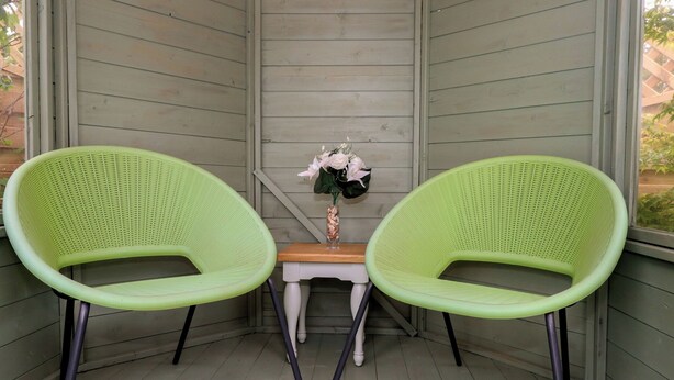 A corner with two green chairs, a small wooden table, and a vase with flowers. - The Coach House (Dorchester)