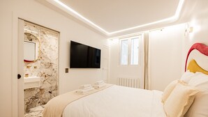 Une chambre avec un mur en marbre, un téléviseur à écran plat, un lit avec une literie blanche, une fenêtre et un radiateur.