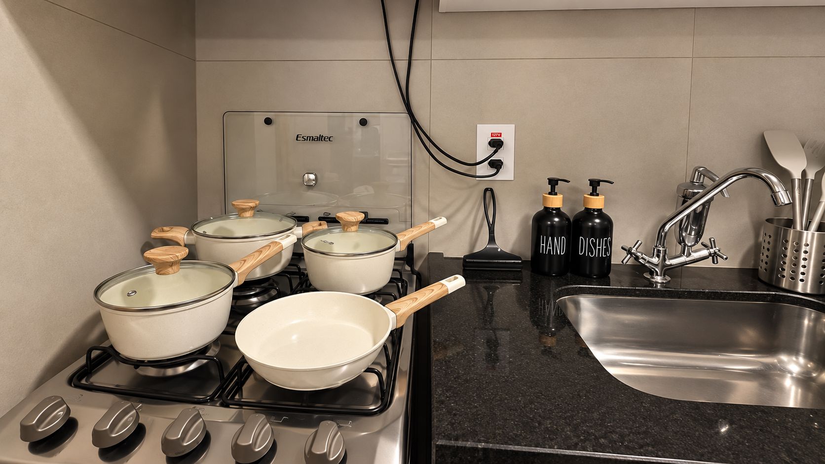 A kitchen with a stove, pots, pans, a sink, and a hand soap dispenser.