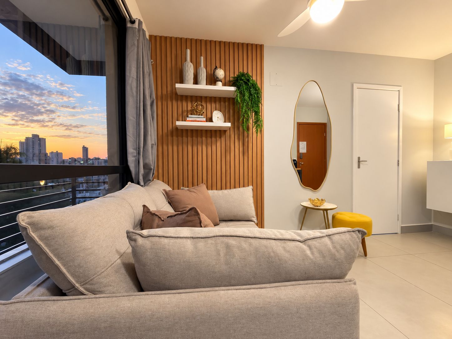 Ein modernes Wohnzimmer mit einer Couch, einem kleinen Beistelltisch, einem Spiegel und Blick auf die Stadt durch ein Fenster.