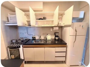 A compact kitchen with a stove, sink, and refrigerator, featuring white cabinets and a black countertop.