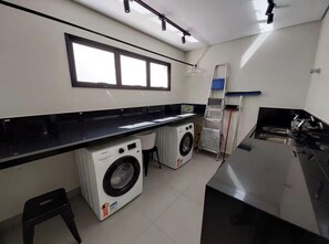 A laundry room with two washing machines, a drying rack, and a large mirror.